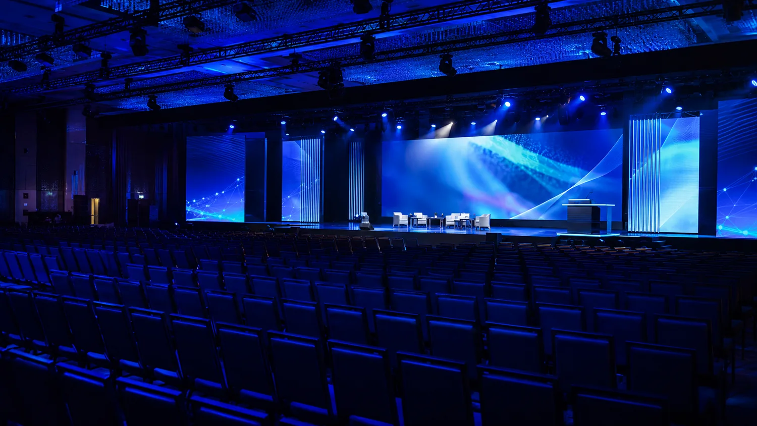 Auditório corporativo com palco, telões e iluminação azul para conferência